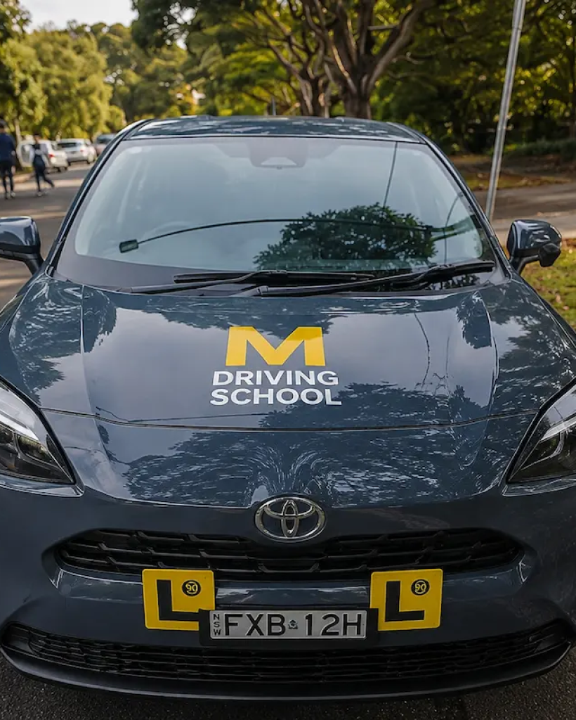 Front view of an M Driving School Toyota learner vehicle with L plates parked on a quiet Australian suburban street, ready for professional driving lessons.